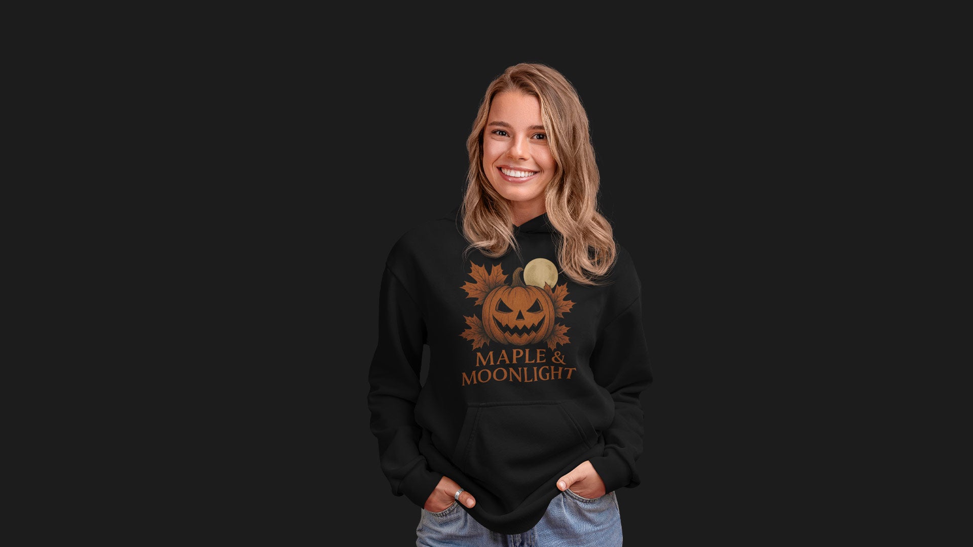 Smiling woman wearing black hoodie with pumpkin, maple leaves and full moon design – cozy seasonal Halloween banner for Canadian Fall collection.